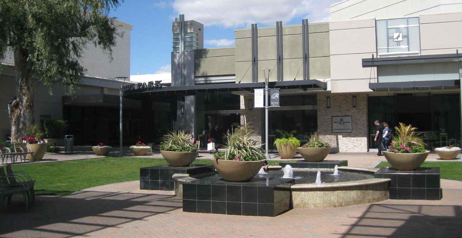 Landscaped courtyard at Biltmore Fashion Park with lawn, planted urns, water feature, and surrounding retail frontages