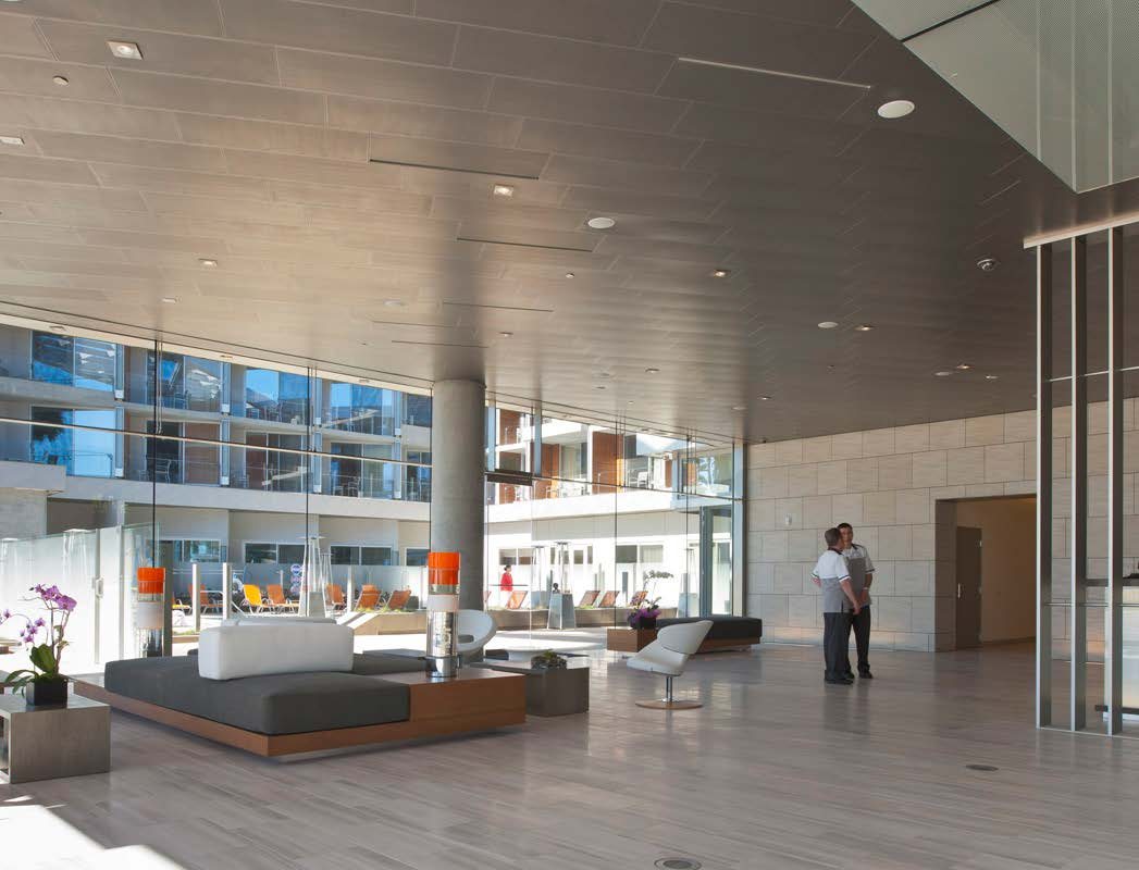 Shore Hotel lobby lounge with a wood-slat ceiling, stone feature wall, orange accent seating, and full-height glazing to the courtyard