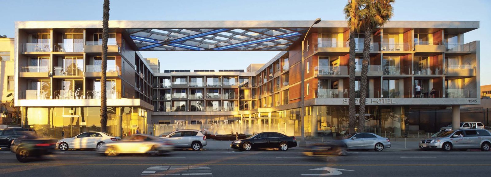 Shore Hotel viewed from Ocean Avenue at dusk with warm interior lighting across four floors of guest-room balconies and traffic passing in the foreground