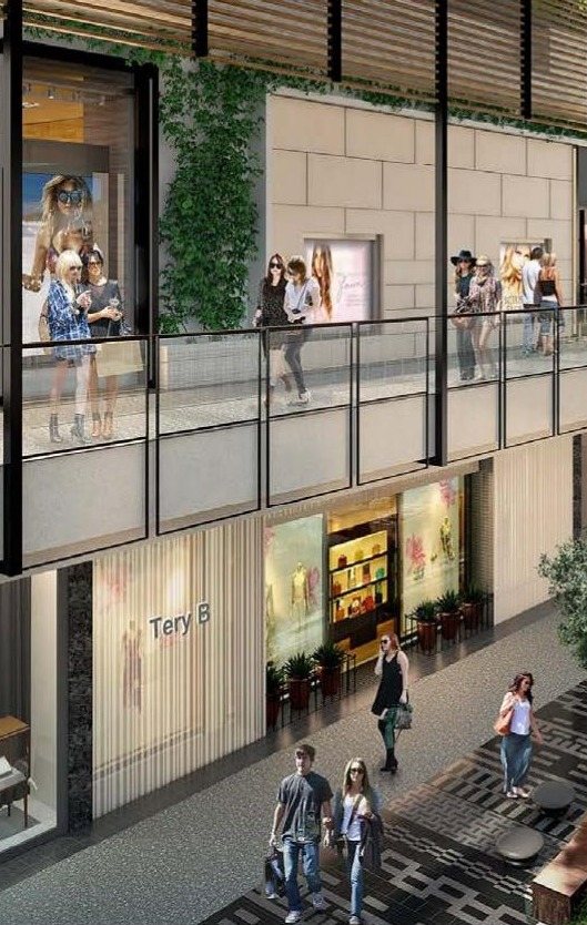 Two-level retail street at Westfield Century City with stone-clad piers, full-height storefront glazing, and shoppers on the upper balcony